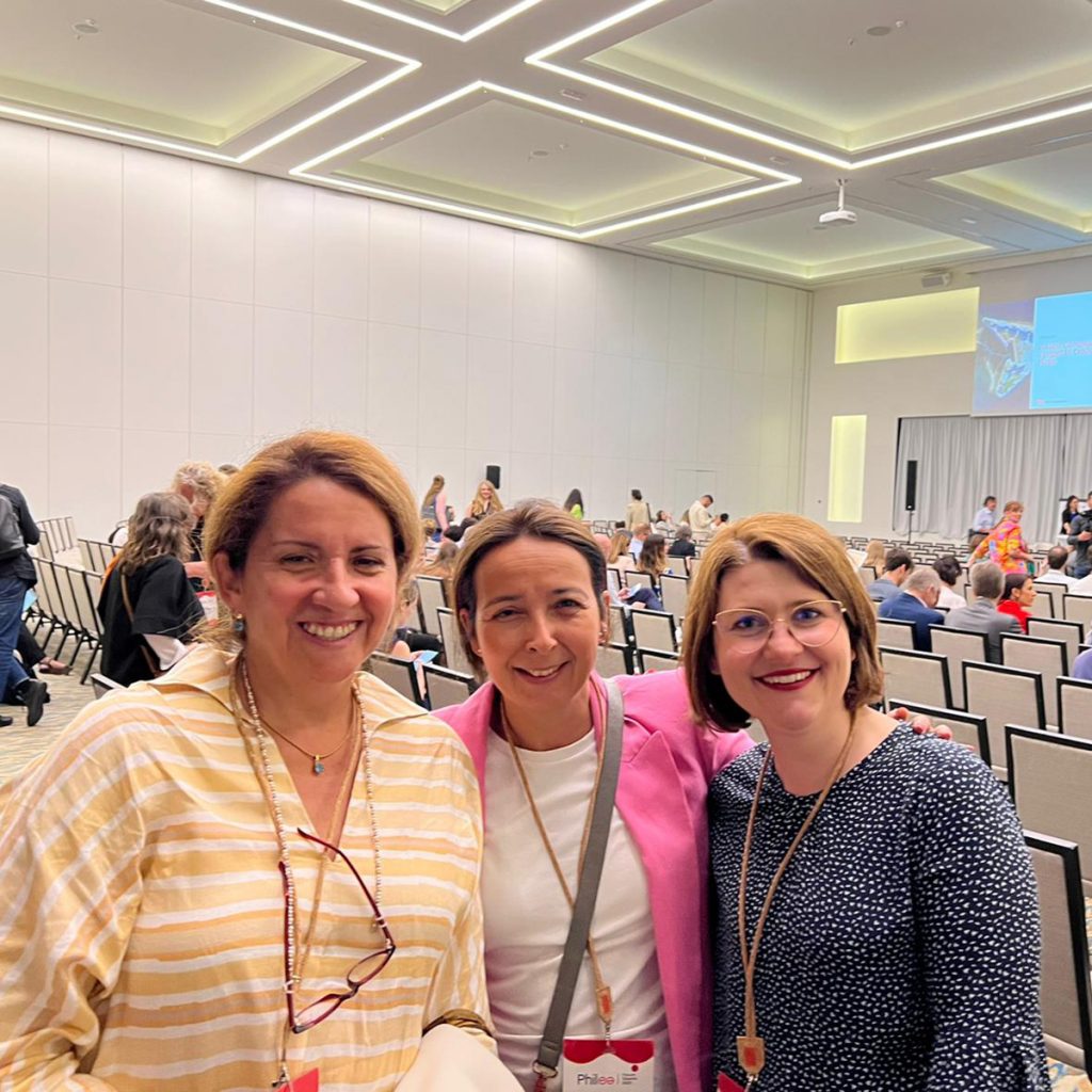 Imagen de tres mujeres de pelo claro, sonriendo mirando a la cámara en un auditorio.En la imagen de izquierda a derecha, Carola Rubia de Fundación Descúbreme, junto a Lourdes Márquez de la Calleja de Fundación ONCE y Anna Königseder de Zero Project. 