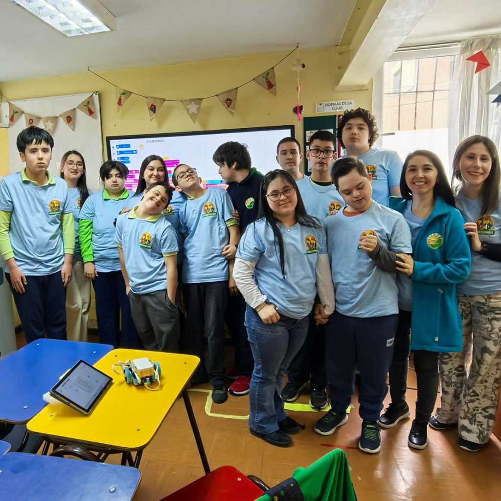 Estudiantes y docentes del Colegio PER SE posan junto a un robot educativo y una pantalla con programación por bloques.
